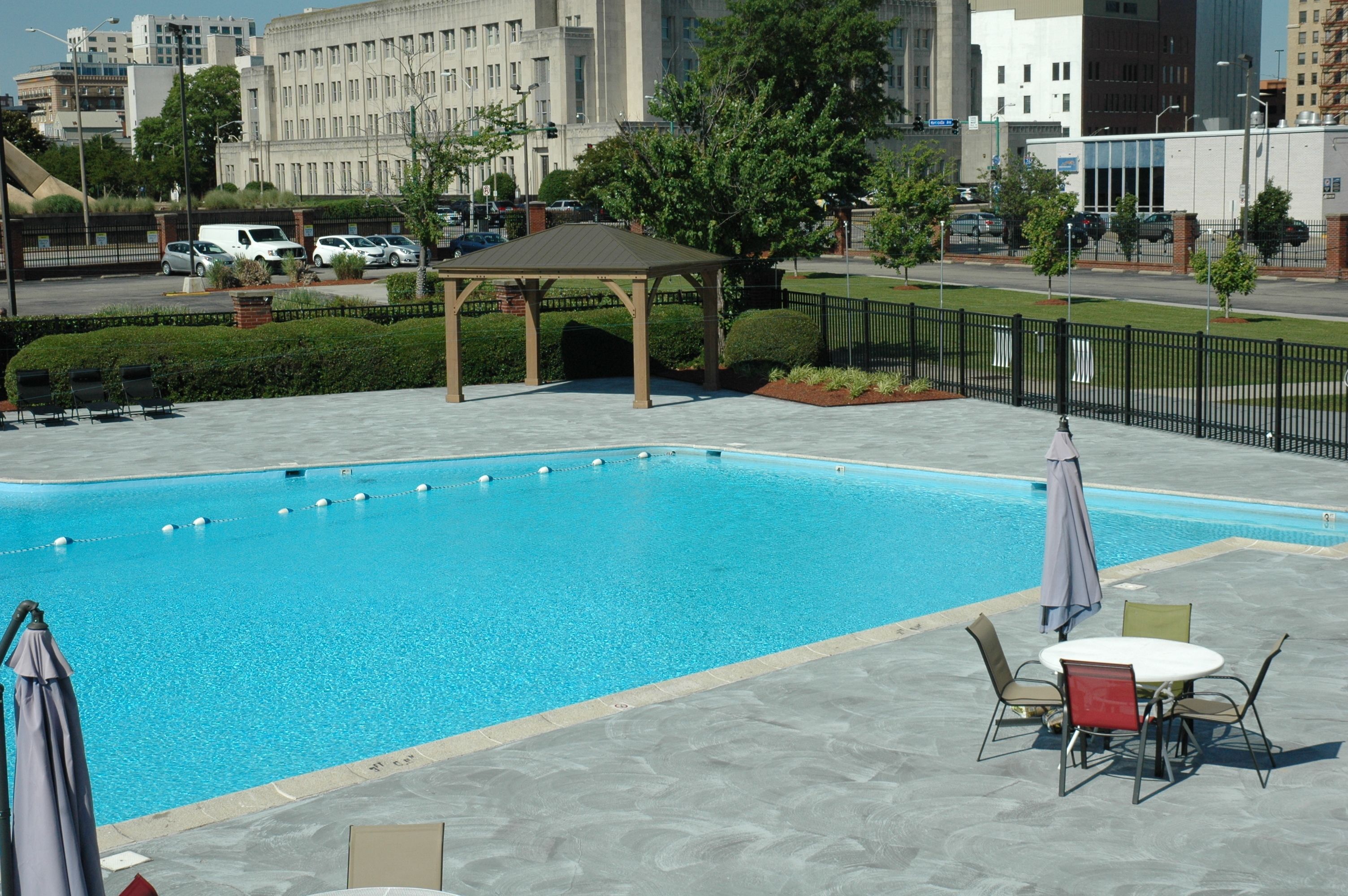 Piscina con un pabellón y zona de estar al aire libre, rodeada de una valla y follaje.