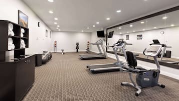 Ein modernes Fitnessstudio mit Laufbändern, Crosstrainern und einer Gewichtbank.
