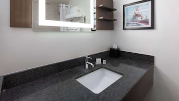 A modern bathroom with a granite countertop, a white sink, a large mirror, and a framed picture on the wall.