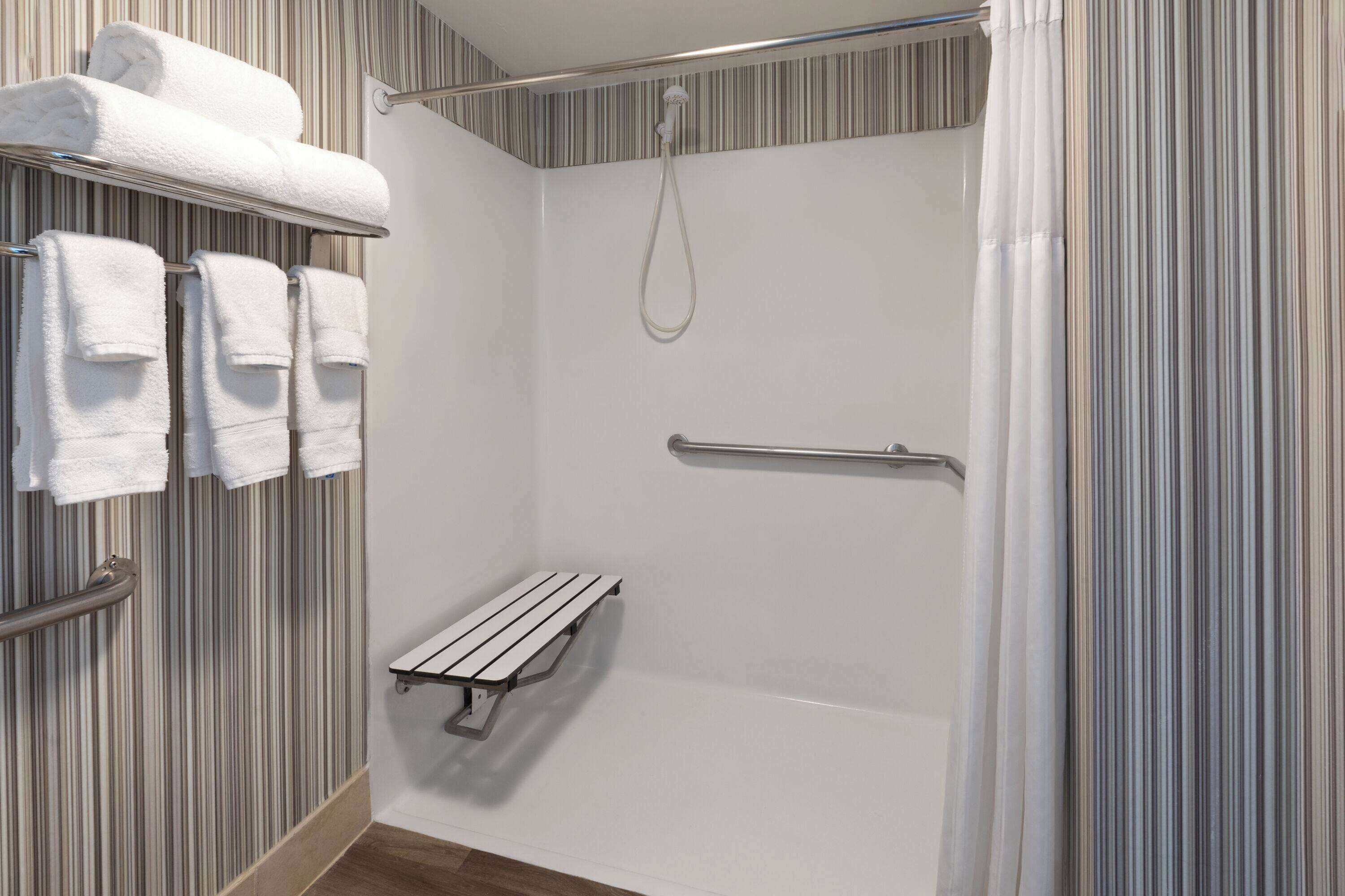 A shower area with a handrail, a bench, and towels on a rack.