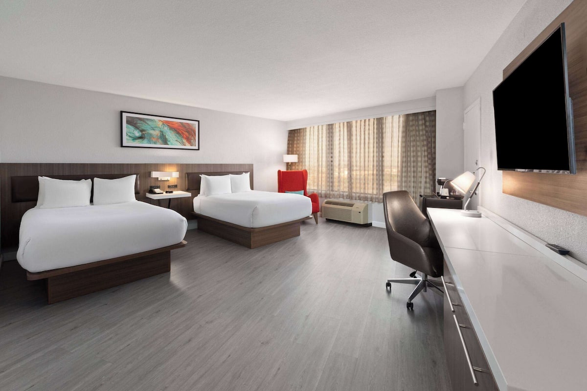 Habitación de hotel con dos camas, un escritorio, una silla, un televisor y una ventana con cortinas.