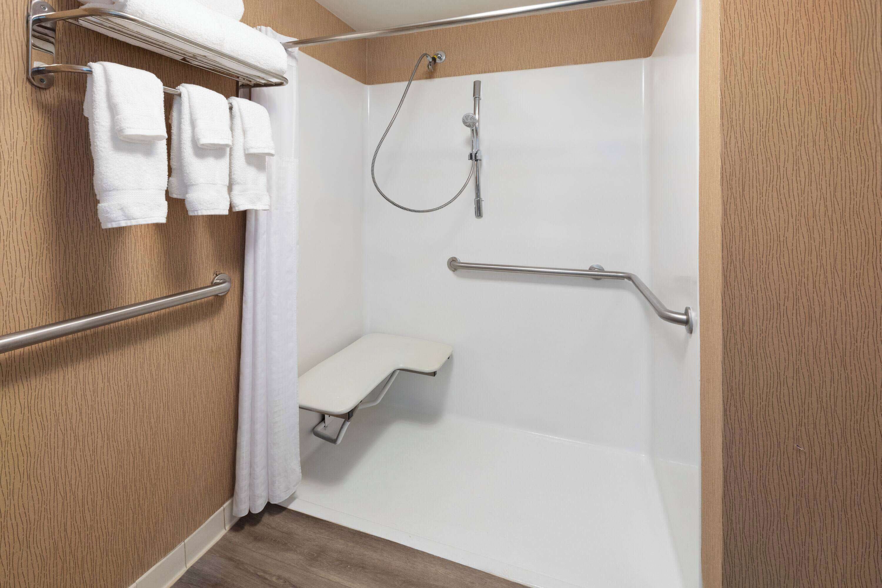 A shower with a grab bar, a towel rack, and a bench.