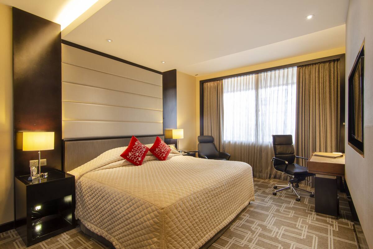 A hotel room with a large bed, a desk, a chair, a TV, and a window with curtains.