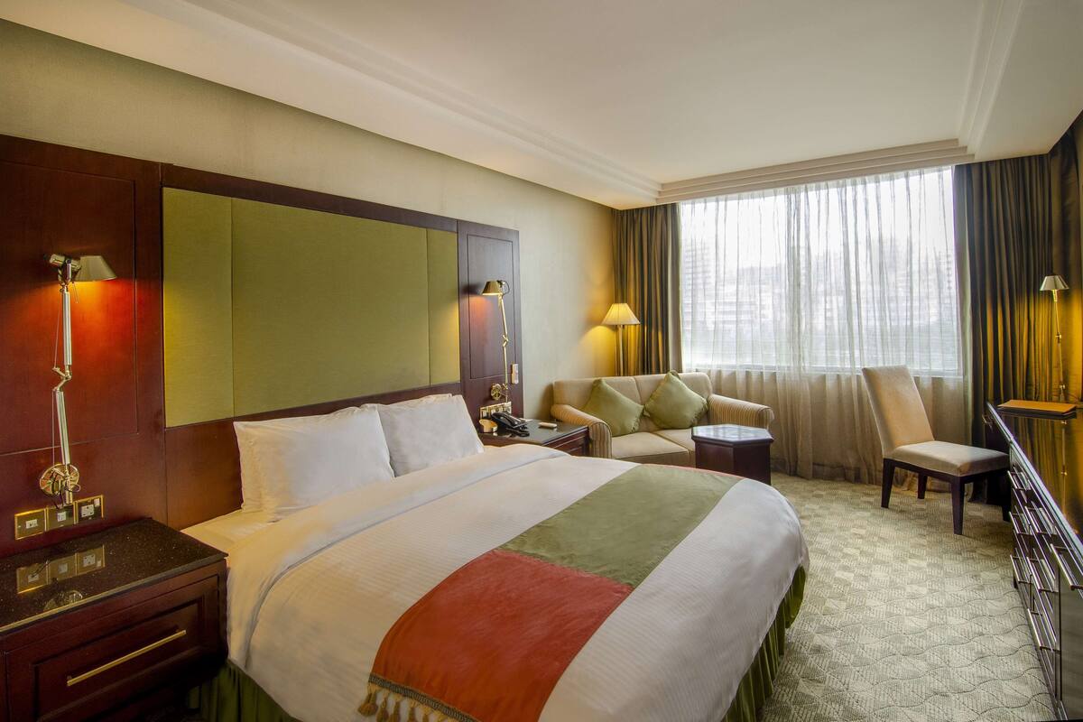 A hotel room with a large bed, a desk, a chair, a sofa, and a window with curtains.