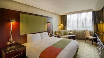Habitación de hotel con una cama grande, un escritorio, una silla, un sofá y una ventana con cortinas.