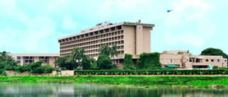 A large building with multiple floors, surrounded by greenery and a body of water.
