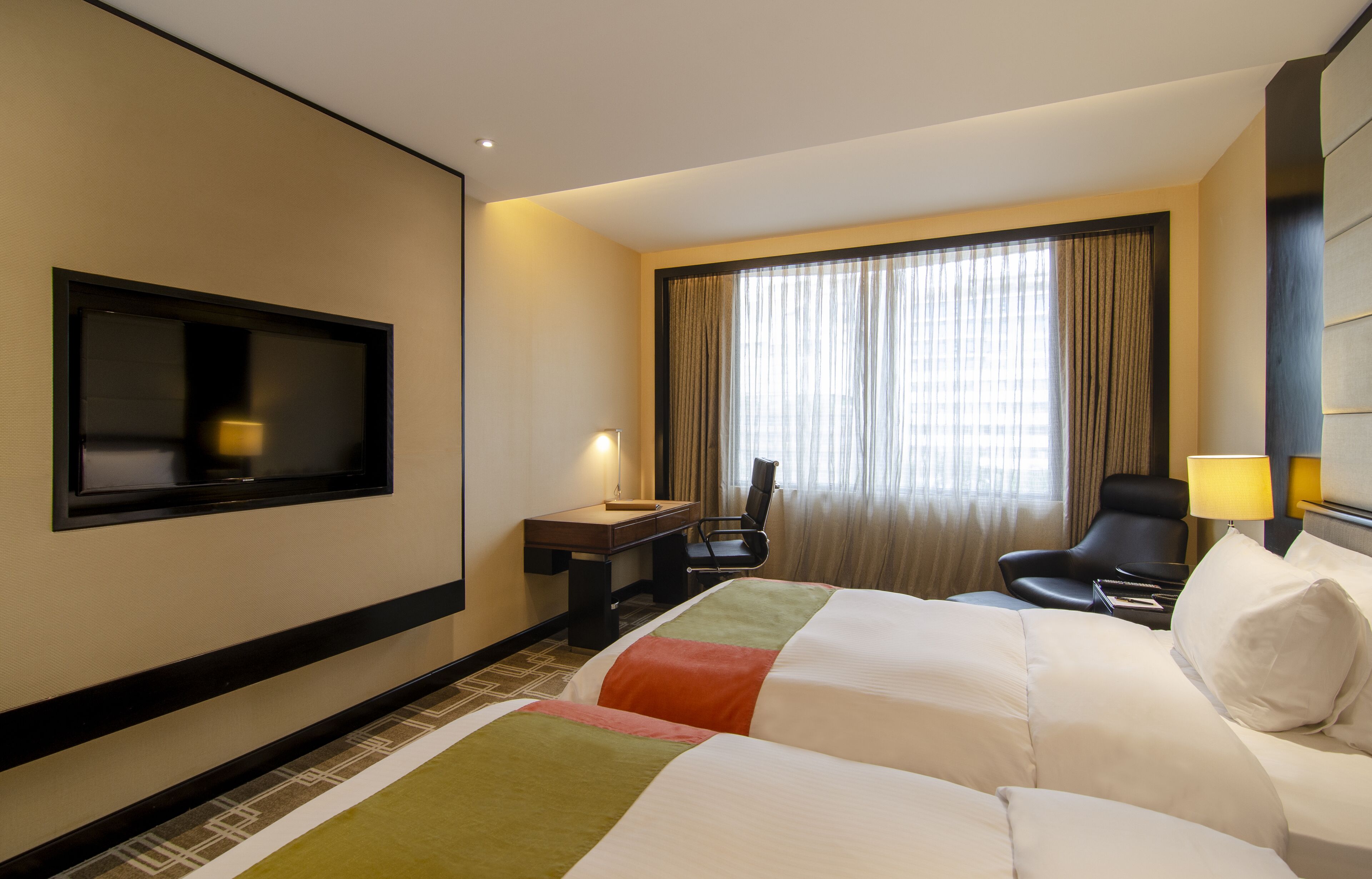 Une chambre d’hôtel avec deux lits, un bureau, une chaise, une télévision et une fenêtre avec des rideaux.