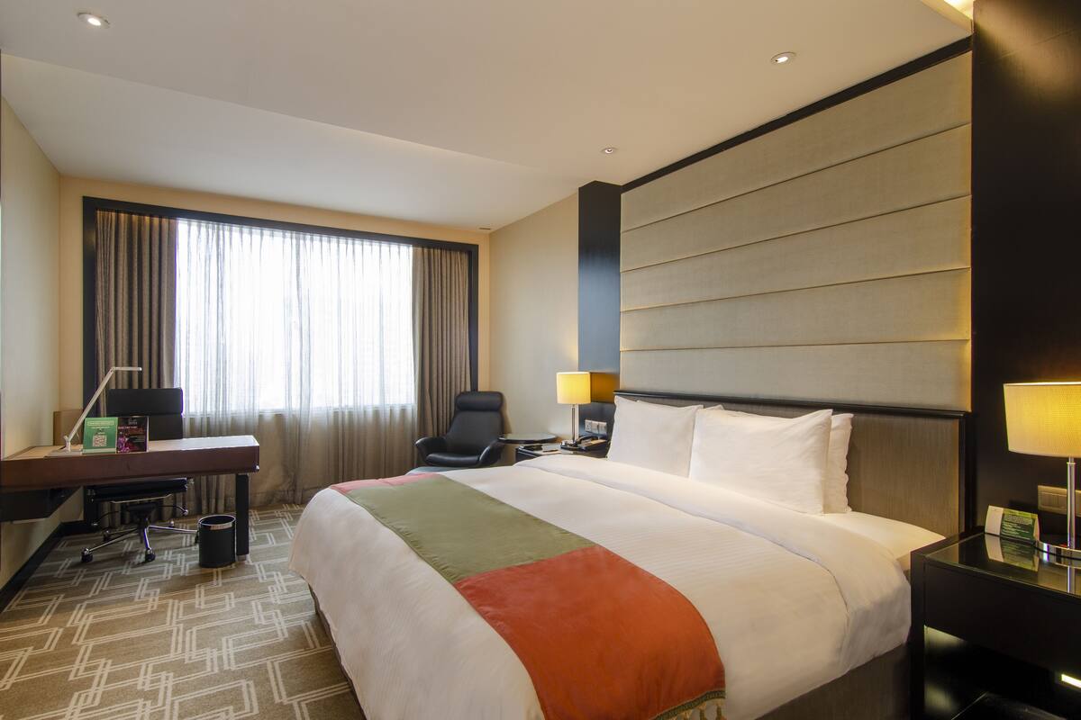 A hotel room with a large bed, a desk with a chair, a TV, and a window with curtains.
