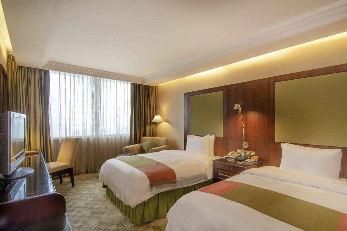 A hotel room with two beds, a desk with a television, a chair, a lamp, and a bedside table with a phone.