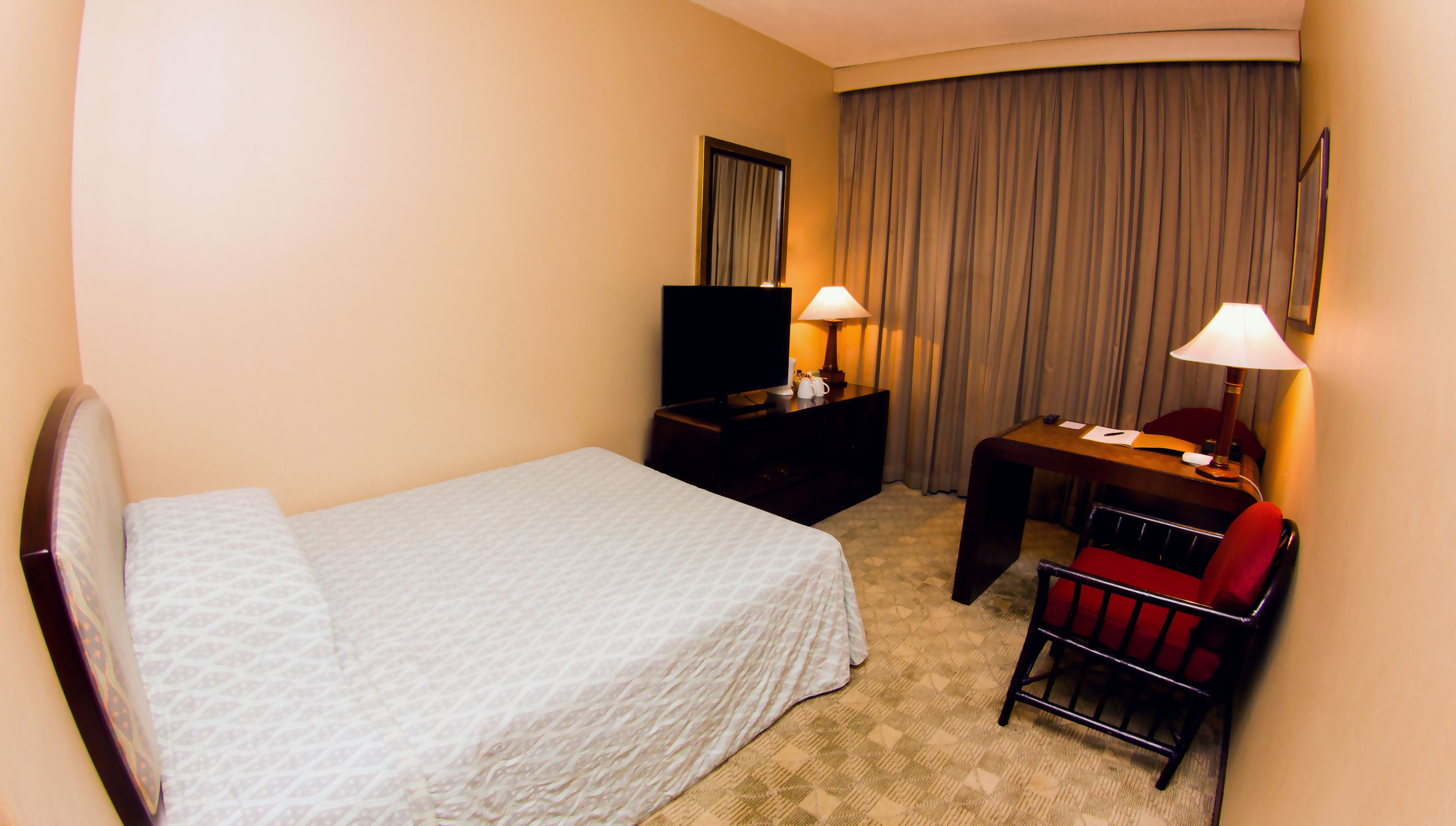 A hotel room with a bed, a desk with a chair, a television, and two lamps.