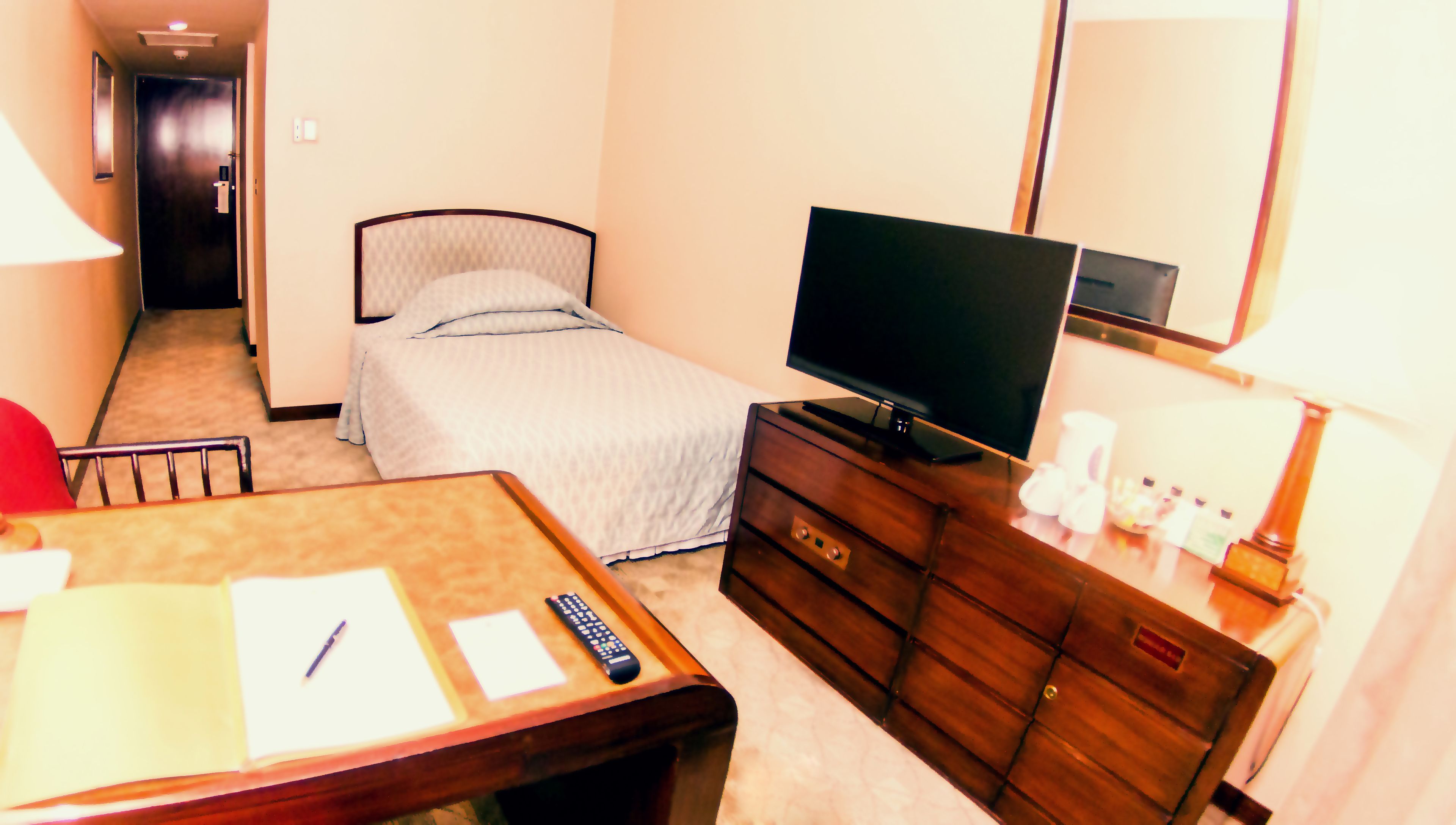 Una habitación de hotel con cama, televisor sobre una cómoda de madera, escritorio con silla y espejo en la pared.