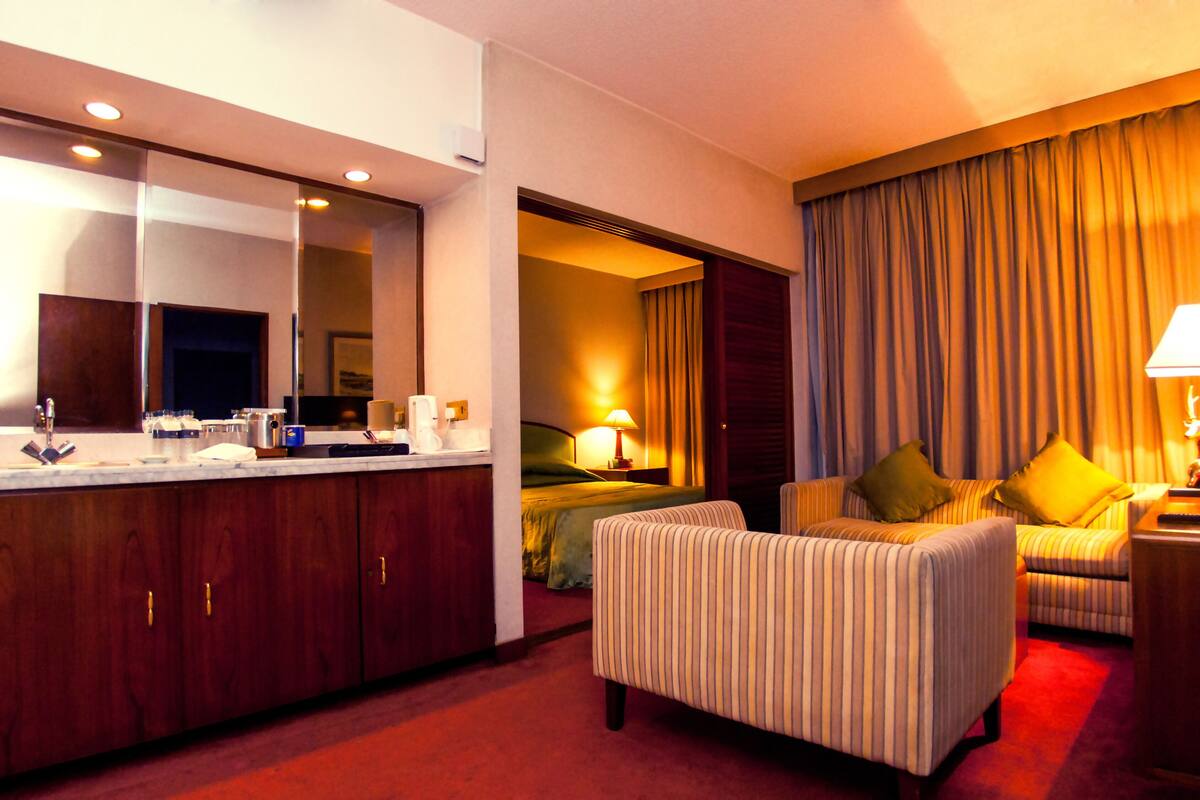 A hotel room with a bed, a sofa, a TV, a lamp, a coffee machine, and a mirror.