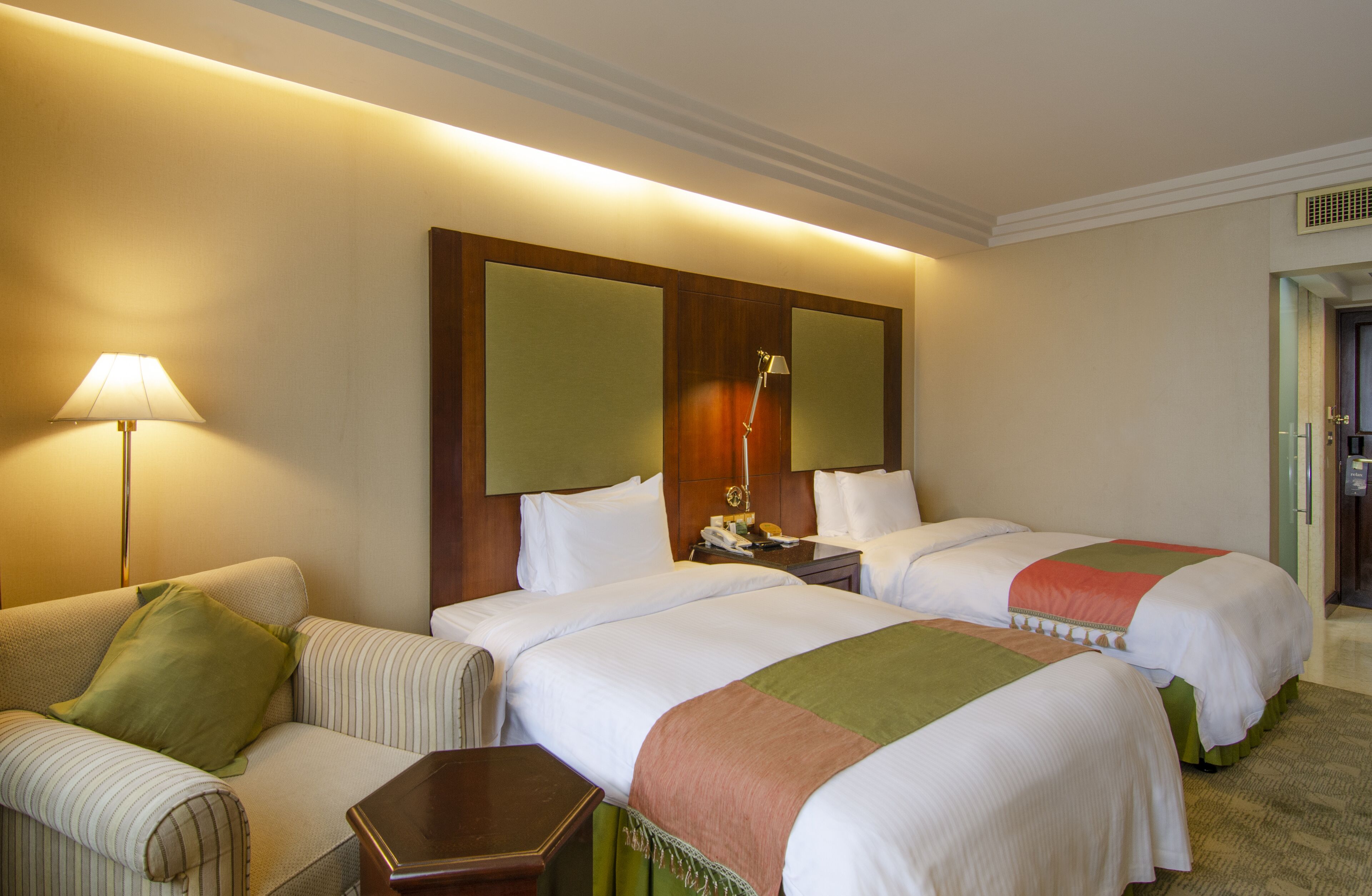 A hotel room with two beds, a sofa, a lamp, and a nightstand.