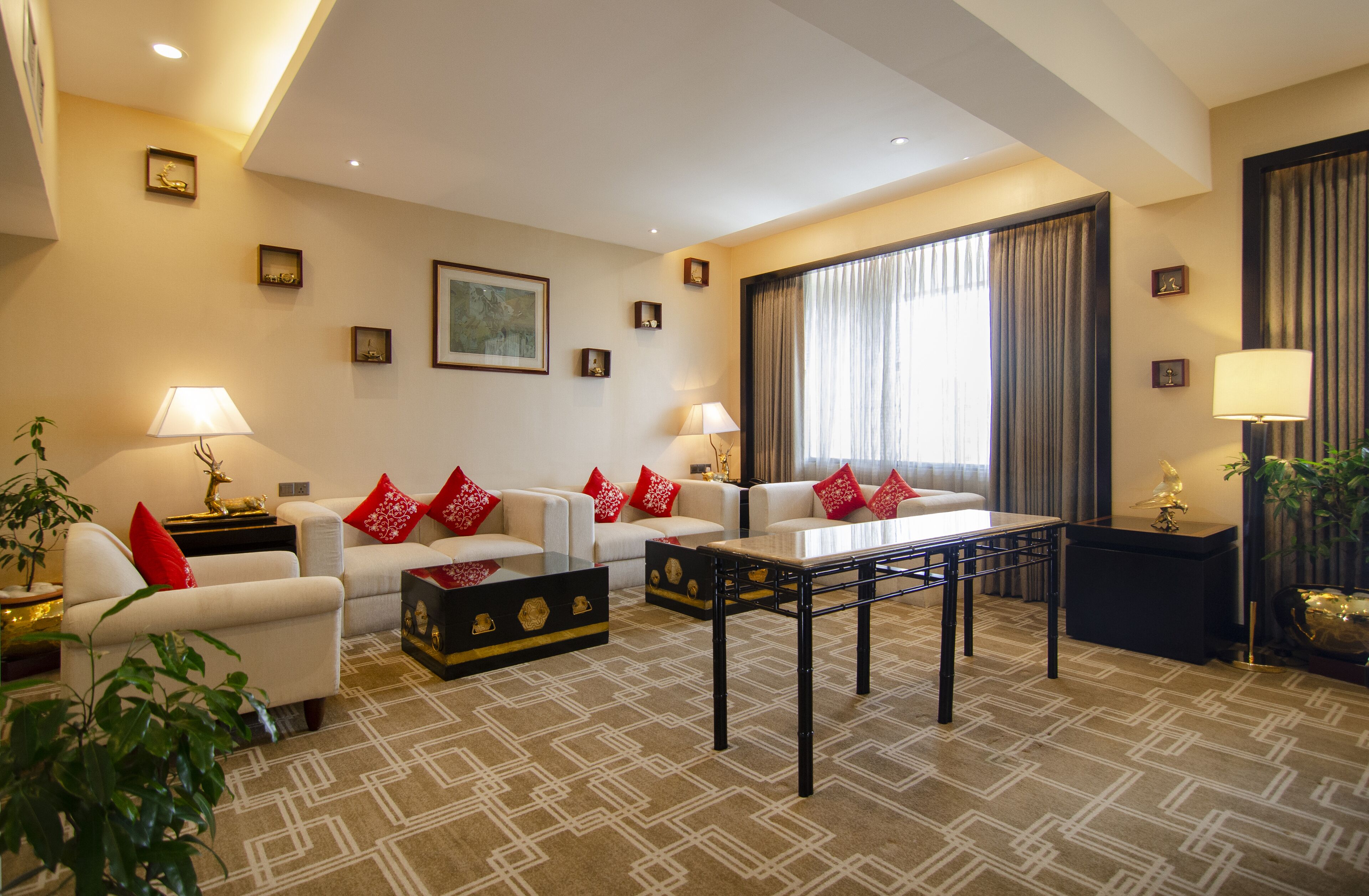 Un salon moderne avec deux canapés blancs, des coussins rouges, une table basse noire et un tapis à motifs.