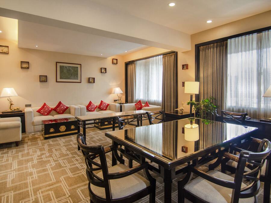 A hotel room with a dining area, a sofa set, and a large window with curtains.