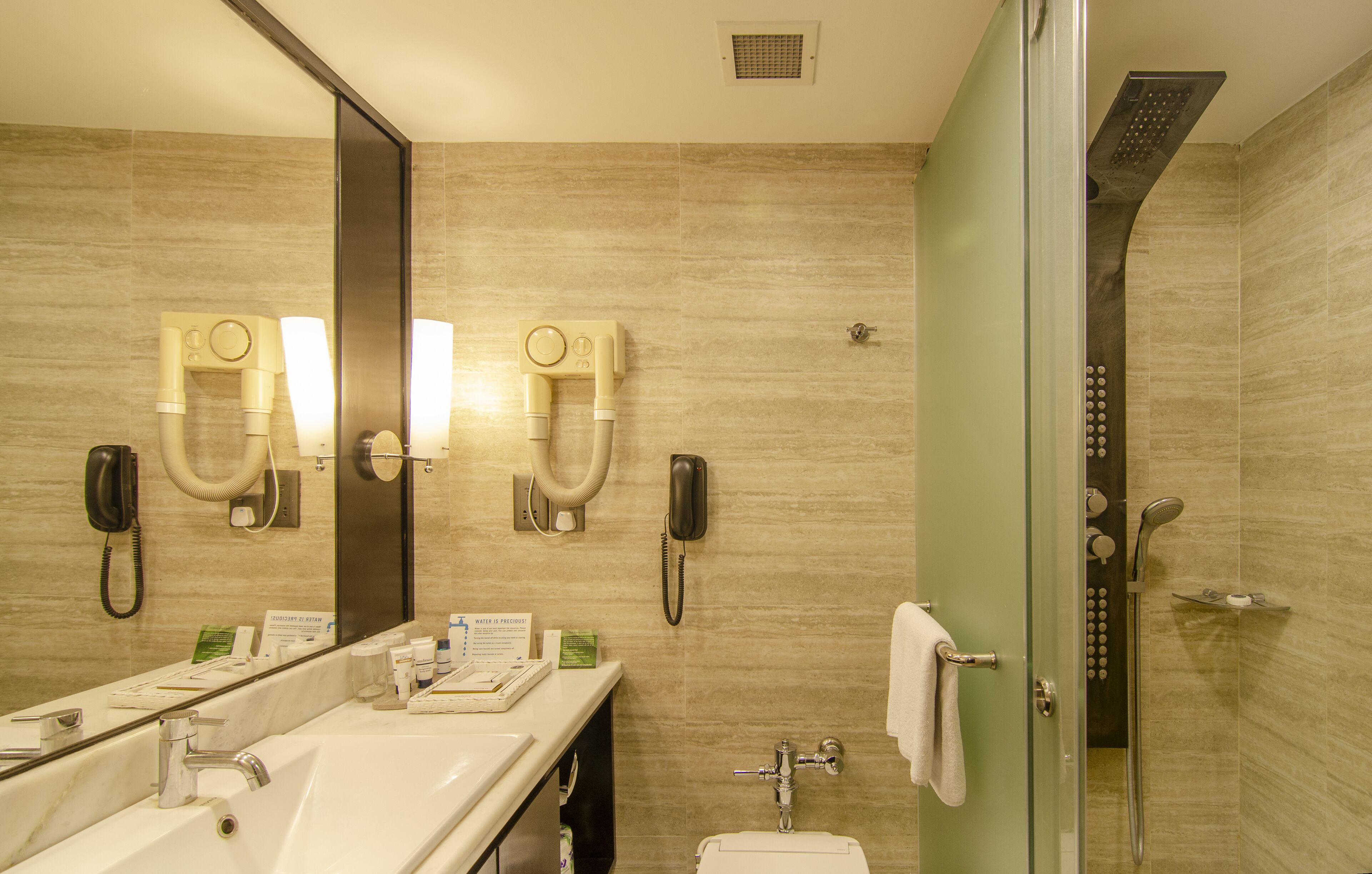 A modern bathroom with a large mirror, dual vanity sinks, a toilet, and a glass-enclosed shower area.