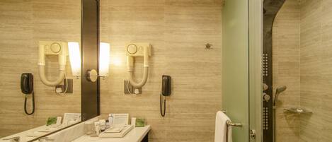 A modern bathroom with a large mirror, dual vanity sinks, a toilet, and a glass-enclosed shower area.