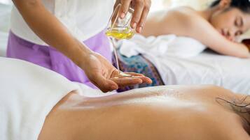 A person receiving a massage with oil being applied to their back.