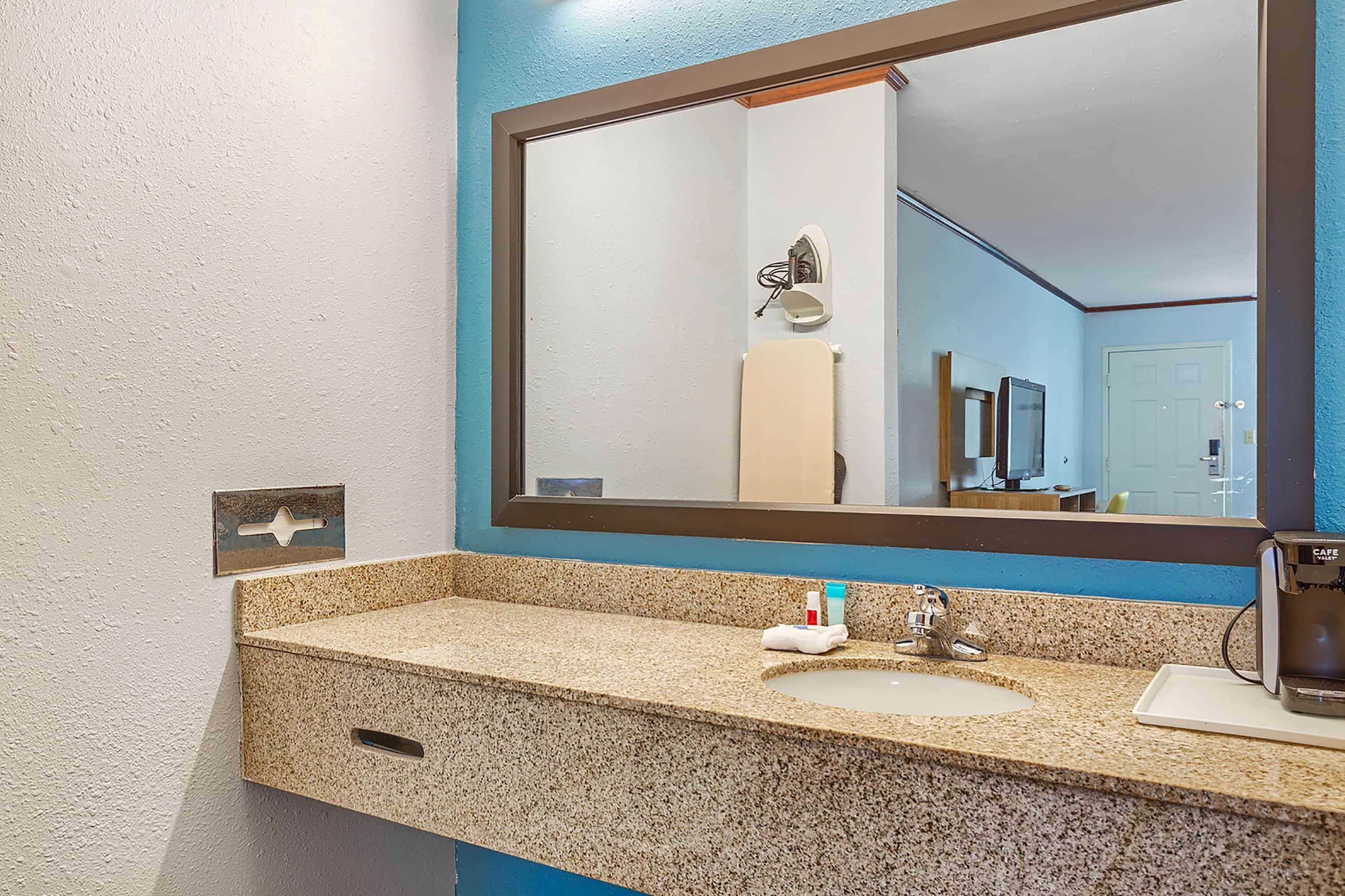 A bathroom with a granite countertop, a sink, a mirror, and a coffee maker.