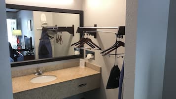 Un baño de hotel con lavamanos de granito, un espejo grande y un perchero con ganchos.