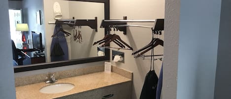 Une salle de bain d’hôtel avec un lavabo en granit, un grand miroir et un porte-serviettes muni de crochets.