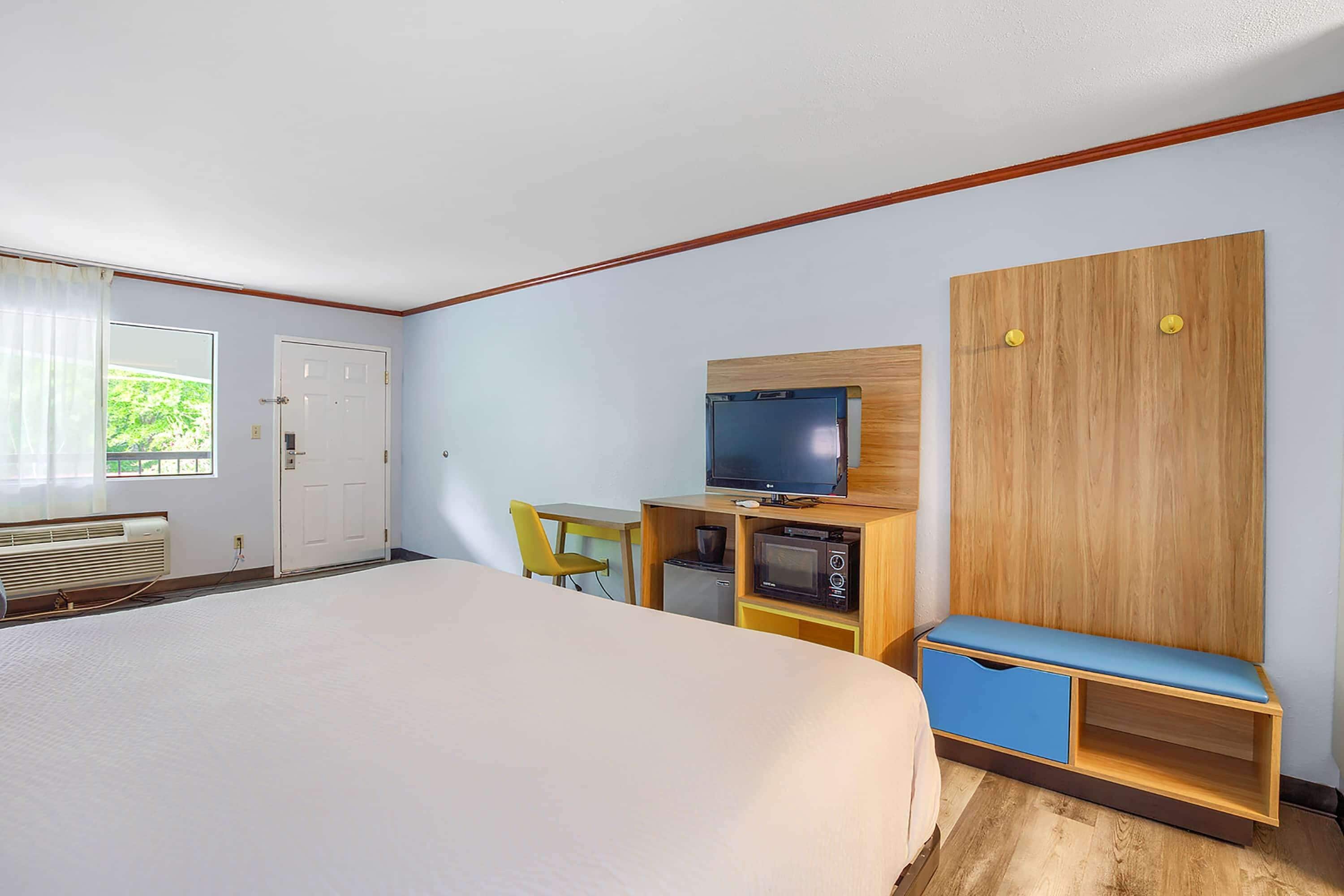 A bedroom with a bed, a desk with a television, a microwave, and a small refrigerator.