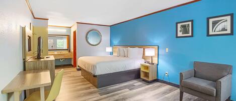 Une chambre d’hôtel comprenant un lit, un bureau, une chaise, une table de chevet et un mur orné de tableaux.