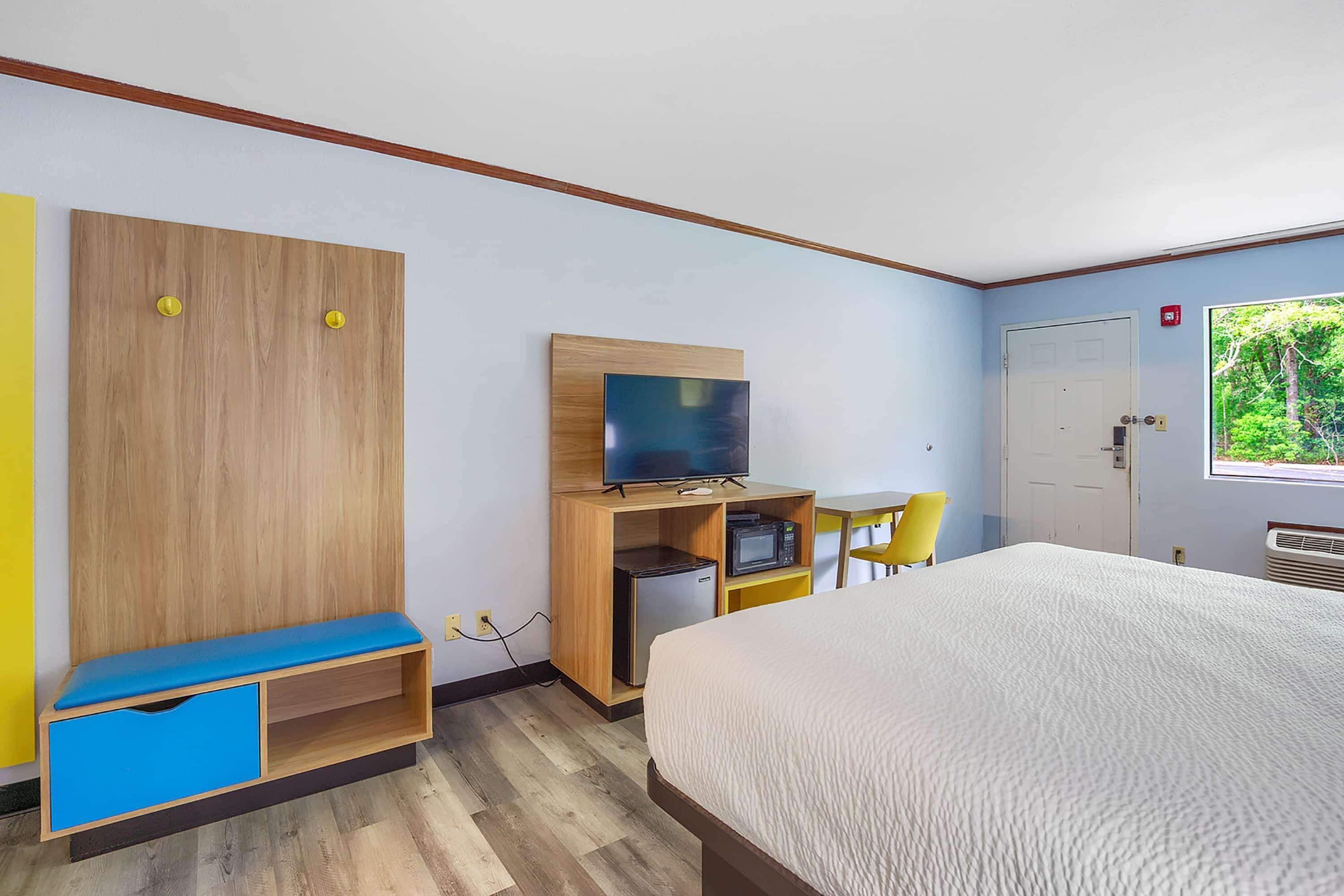 A hotel room with a bed, a TV on a wooden stand, a small desk with a chair, and a wardrobe.