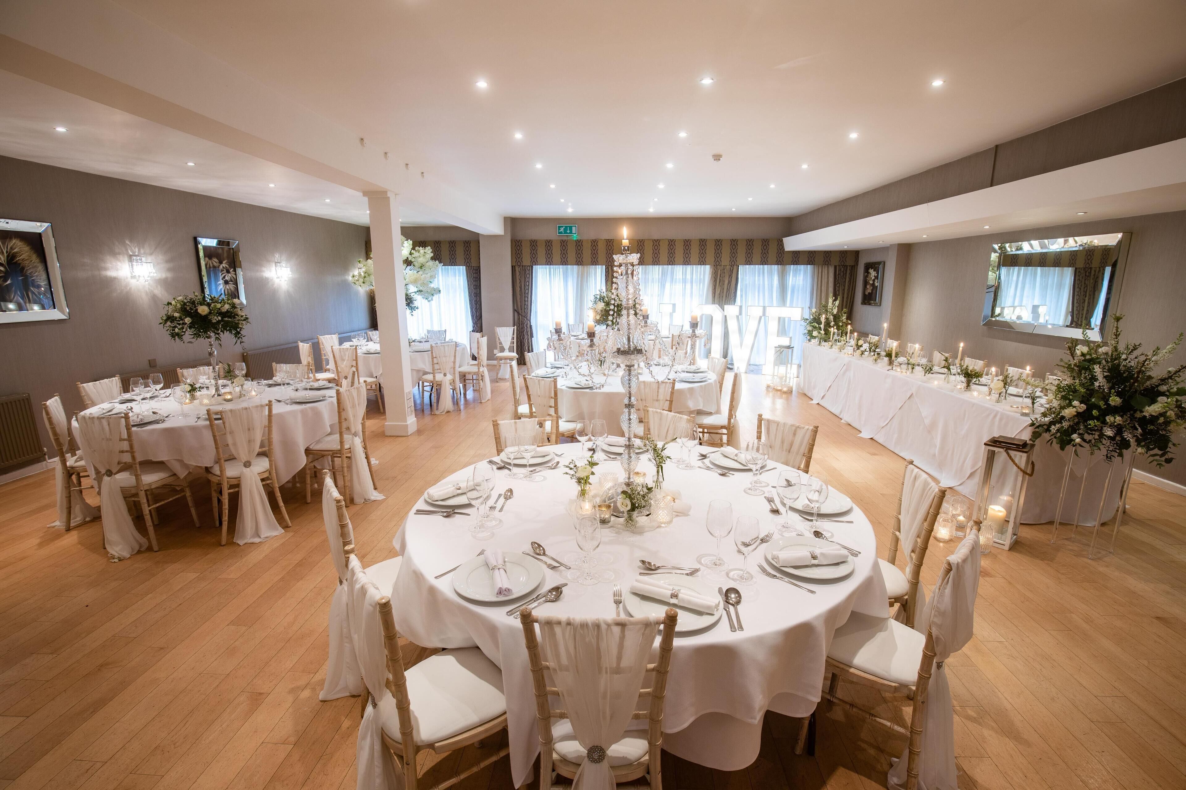 Une salle de banquet avec des tables rondes, des nappes blanches et des centres de table floraux.