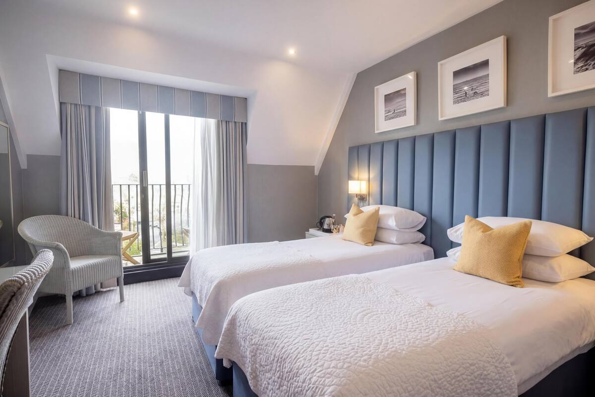 Ein Hotelzimmer mit zwei Betten, einem Sessel, einem Nachttisch und Blick ins Freie.