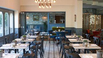 A restaurant with a patterned floor, tables with chairs, a bar area, and a decorative wall with a painting.