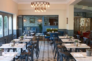A restaurant with a patterned floor, tables with chairs, a bar area, and a decorative wall with a painting. - Best Western Plus The Connaught Hotel & Spa (Bournemouth)