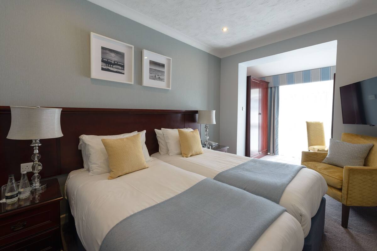 Ein Hotelzimmer mit zwei Betten, einem Nachttisch mit Lampe, einem Sessel und einem Fernseher.