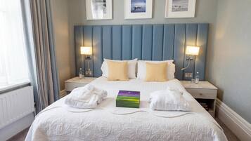 Una habitación de hotel con una cama grande, dos mesitas de noche, un cabecero y tres cuadros enmarcados en la pared.