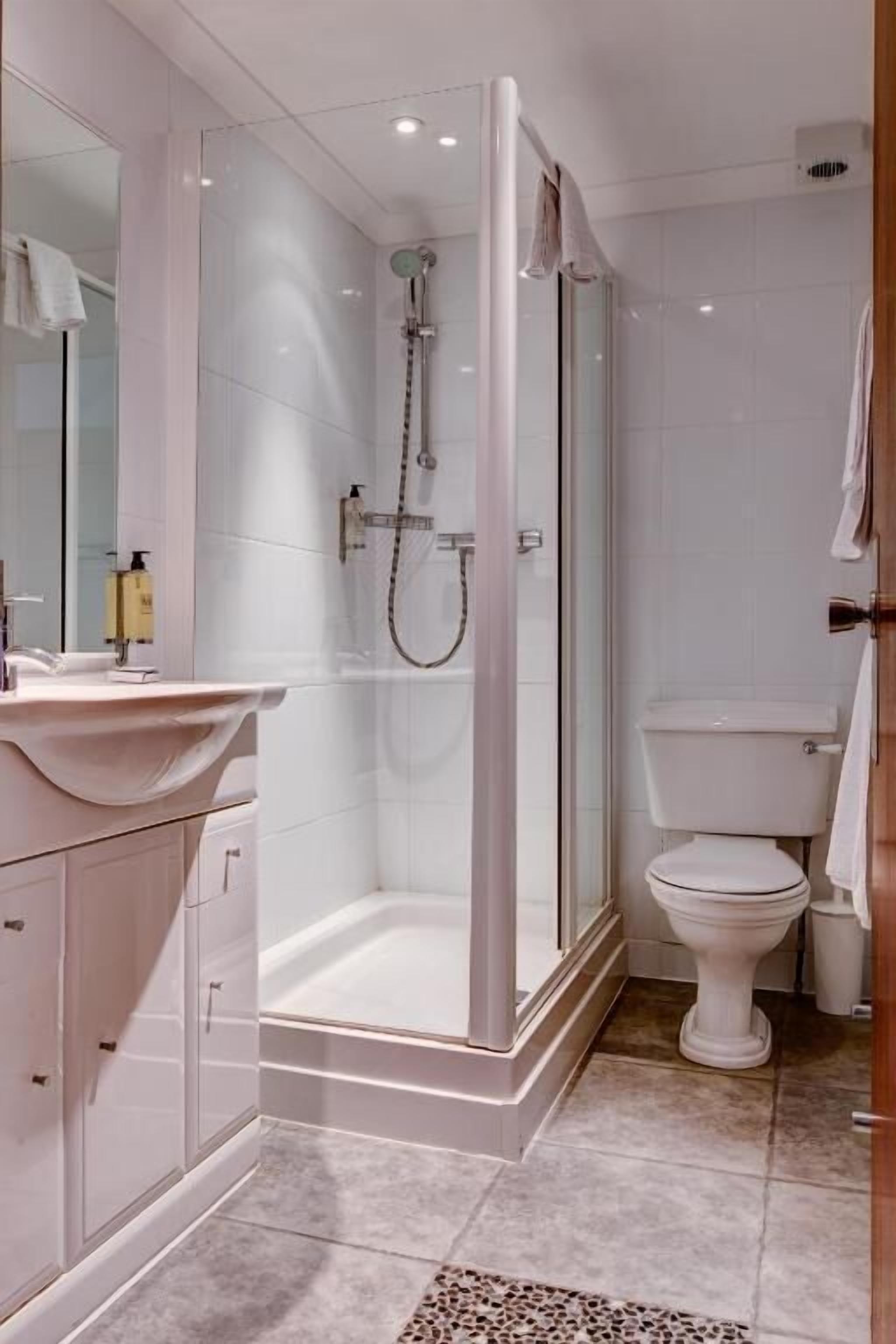 Un baño moderno con ducha envuelta en vidrio, inodoro blanco y tocador con lavamanos.
