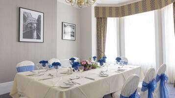 Ein Esszimmer mit einem langen Tisch, der für eine Mahlzeit gedeckt ist, Stühle mit blauen Bändern und gerahmten Bildern an der Wand.