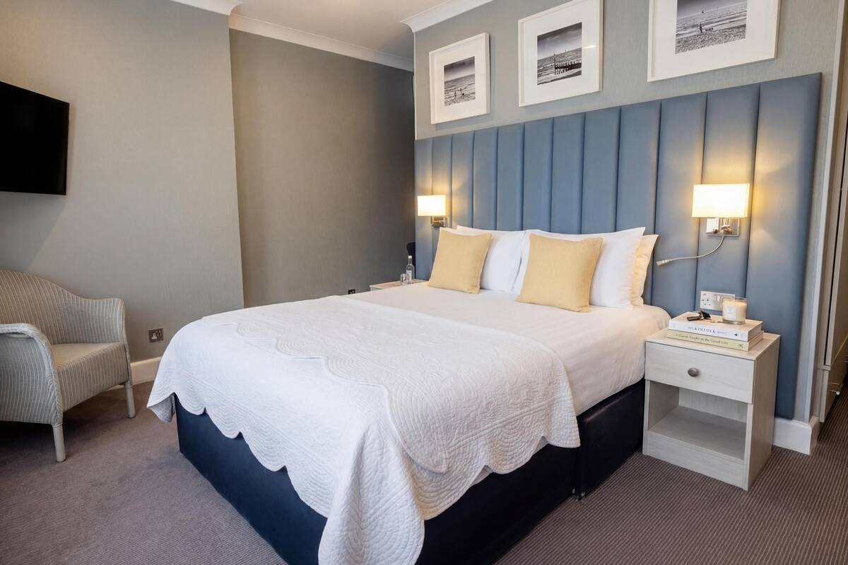 Ein Hotelzimmer mit Bett, Nachttischen, einem Sessel und Wandbildern.