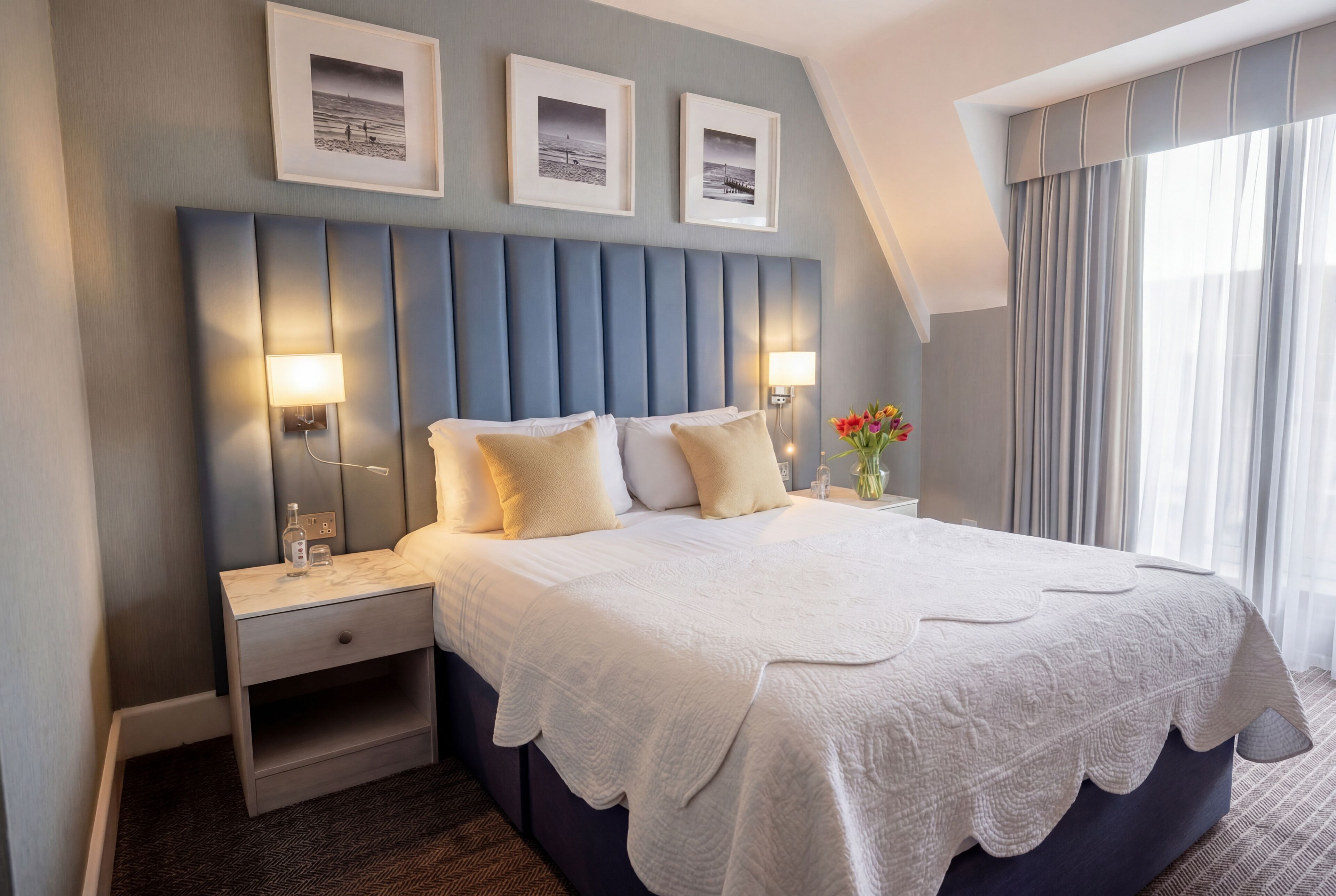 Ein modernes Hotelzimmer mit einem großen Bett, zwei Nachttischen, einer Kopfteil und gerahmten Bildern an der Wand.
