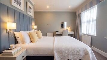 A neatly arranged bedroom with a large bed, bedside lamps, a desk, and a mirror.