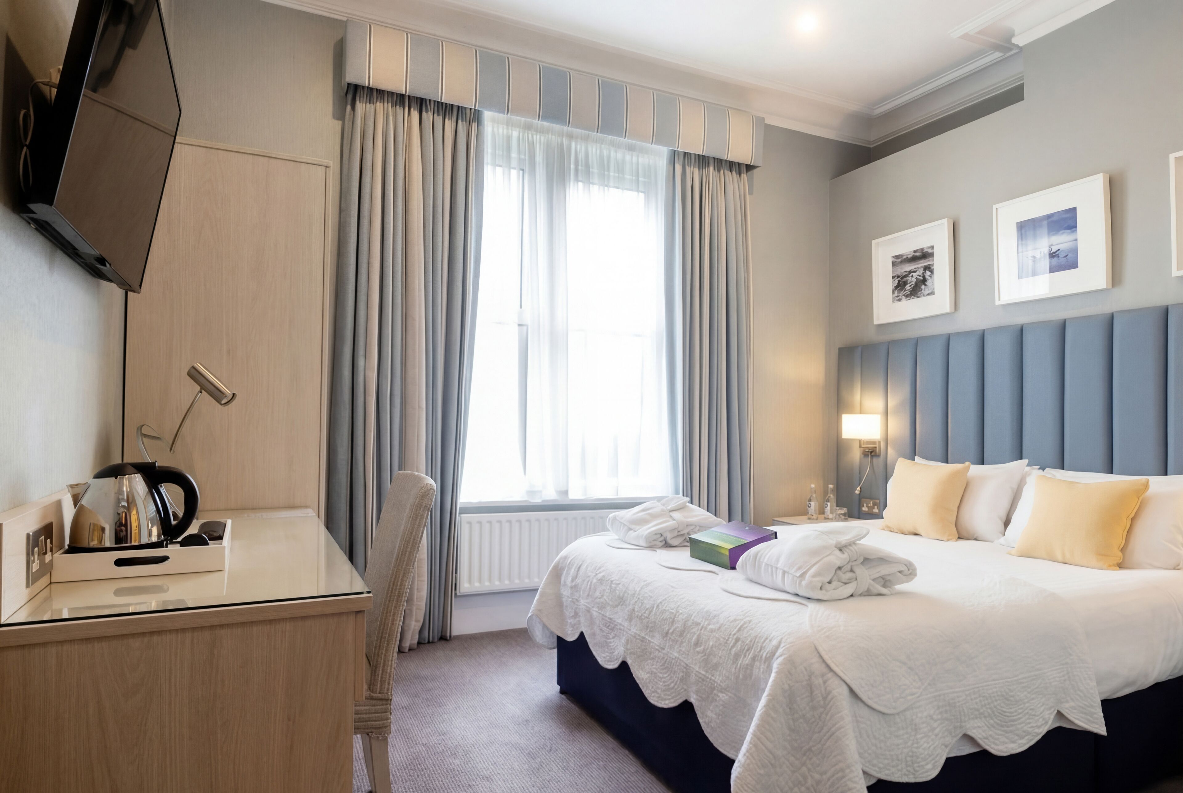 A hotel room with a bed, a desk, a chair, a TV, and a window with curtains.