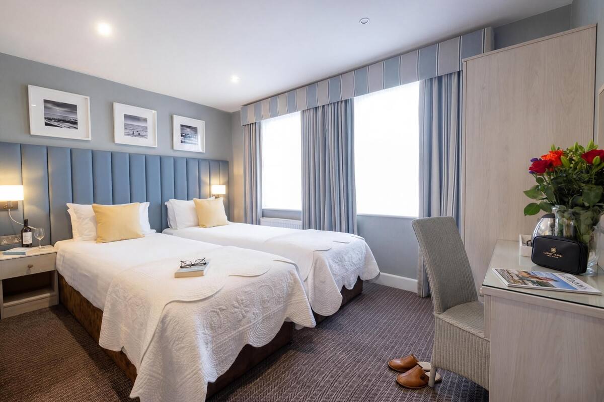 Ein Hotelzimmer mit zwei Betten, einem Schreibtisch, einem Stuhl, einem Nachttisch und einem Fenster mit Vorhängen.