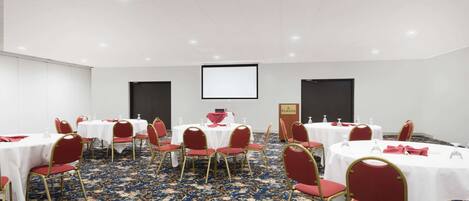 A conference room with round tables, red chairs, white tablecloths, and a projector screen.