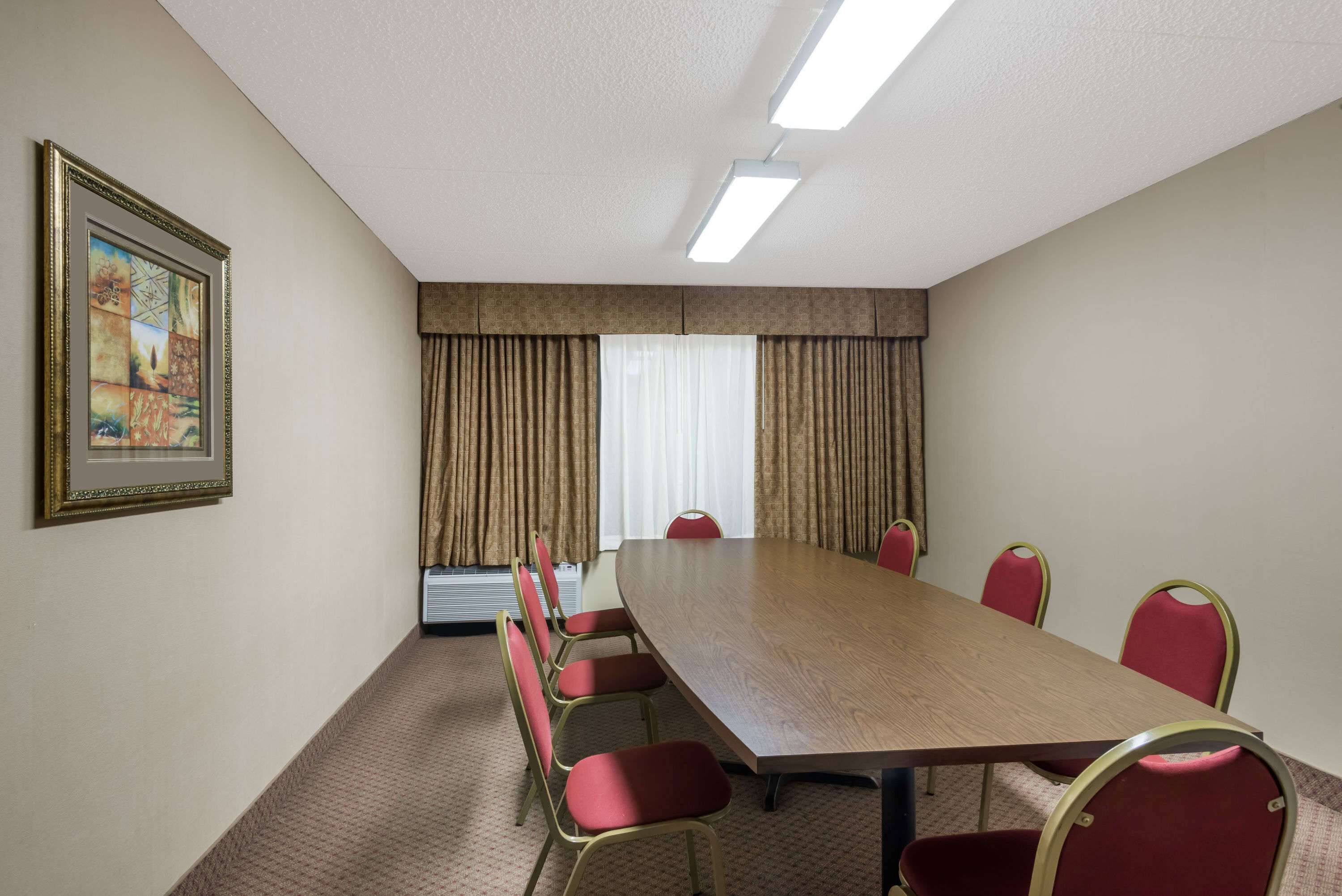 A conference room with a long table and red chairs, a framed picture on the wall, and a window with curtains.