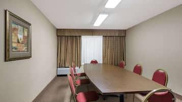 A conference room with a long table and red chairs, a framed picture on the wall, and a window with curtains.