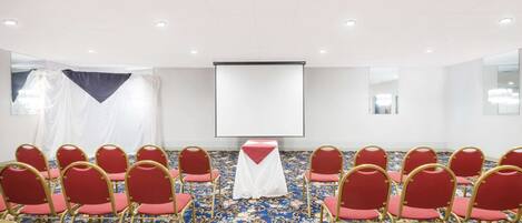 A conference room with rows of red chairs, a white table with a red cloth, and a projector screen.