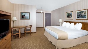 A hotel room with a bed, a TV, a desk, and two lamps. - Ramada by Wyndham Watertown/Thousand Islands NY (Watertown)