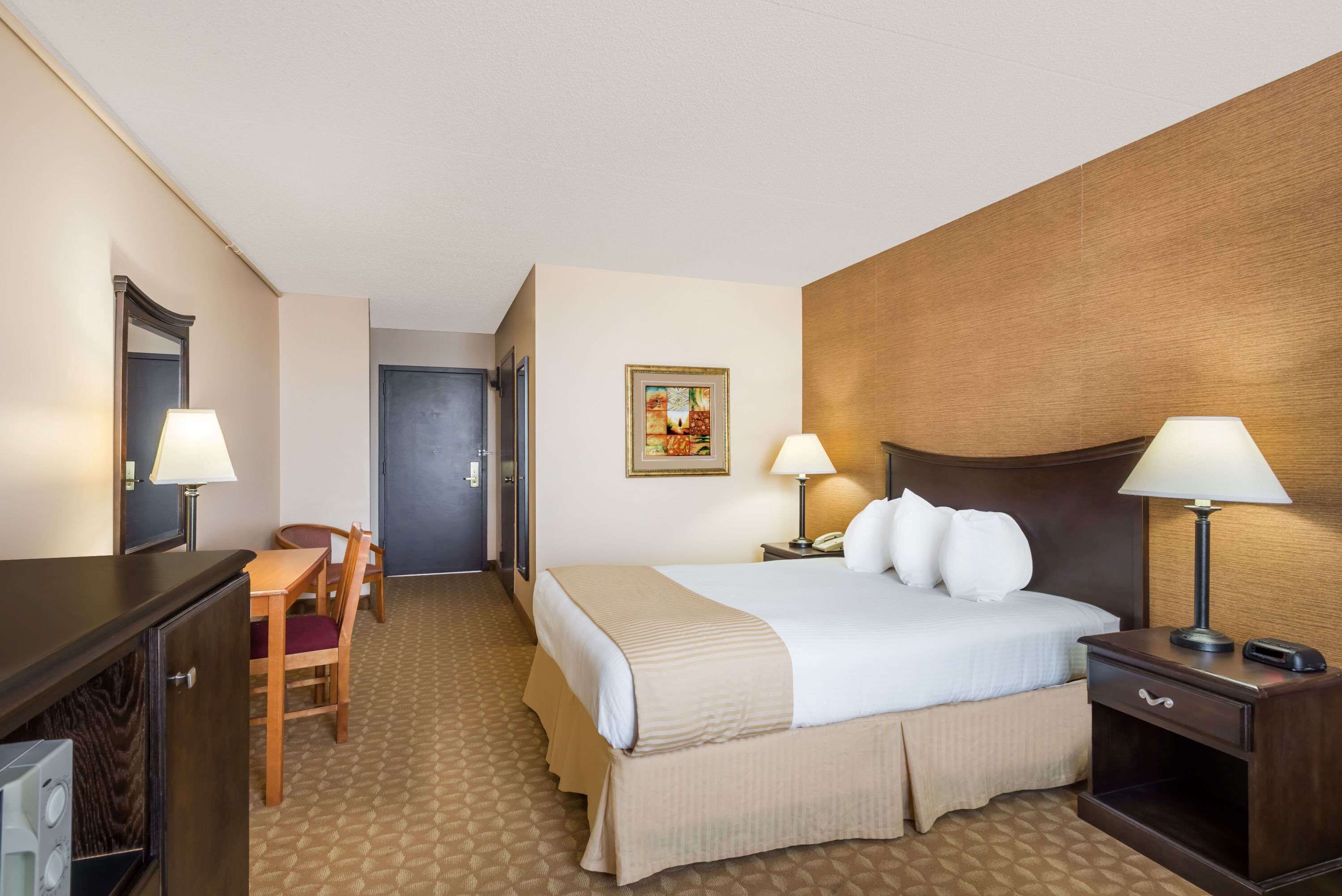 A hotel room with a bed, bedside tables, a desk with a chair, a mirror, and a door.