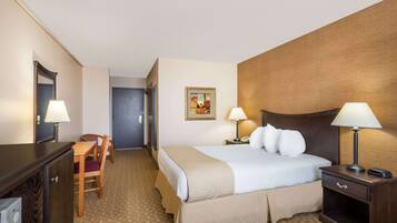 A hotel room with a bed, bedside tables, a desk with a chair, a mirror, and a door.