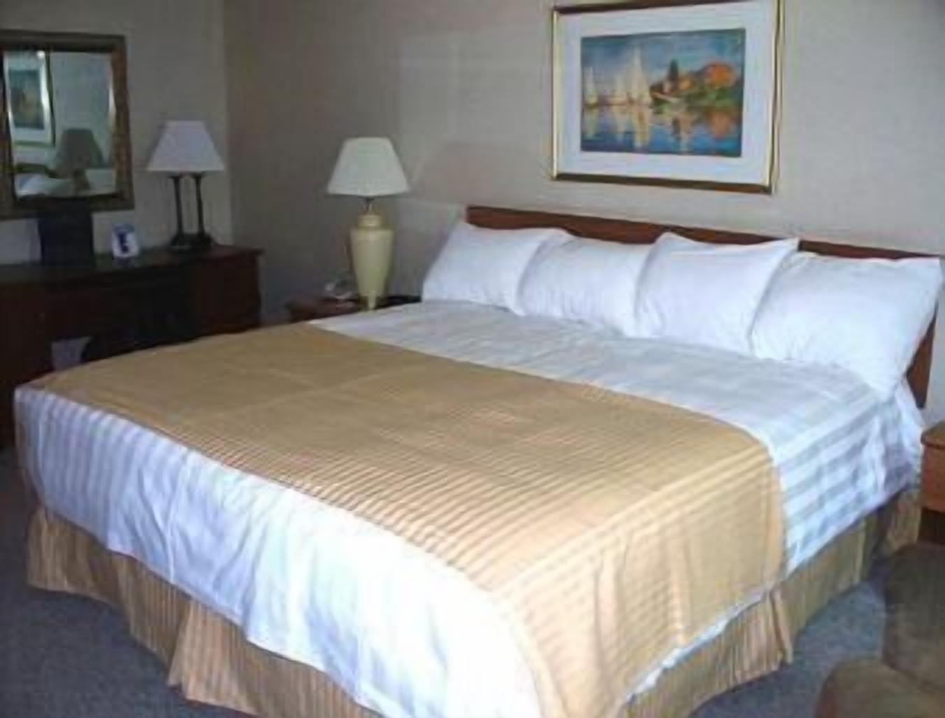A neatly made bed with white linens and a beige bedspread in a hotel room.