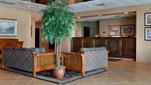 A lobby with a reception desk, seating area, and a large potted plant. - Ramada by Wyndham Watertown/Thousand Islands NY (Watertown)